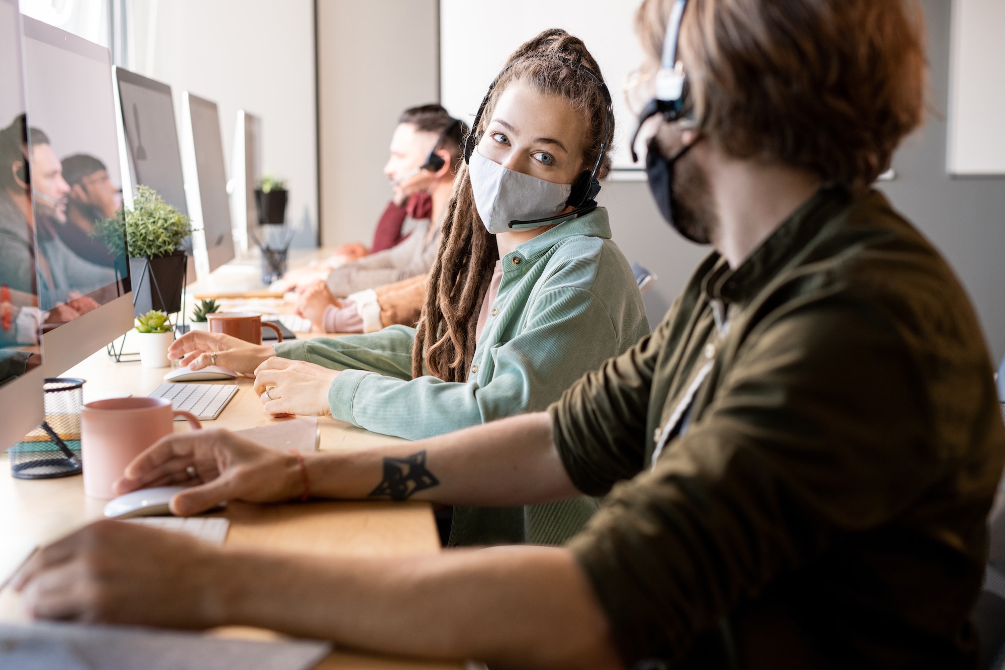 Female operator of call center in protective mask consulting with male colleague